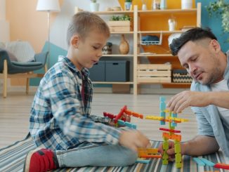 Happy kid is playing with joyful dad using construction blocks enjoying funny game at home on floor having fun and talking. Childhood and people concept.