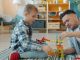 Happy kid is playing with joyful dad using construction blocks enjoying funny game at home on floor having fun and talking. Childhood and people concept.