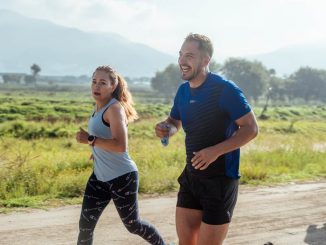 Two adults running on a rural dirt path, enjoying a sunny day outdoors.