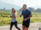 Two adults running on a rural dirt path, enjoying a sunny day outdoors.